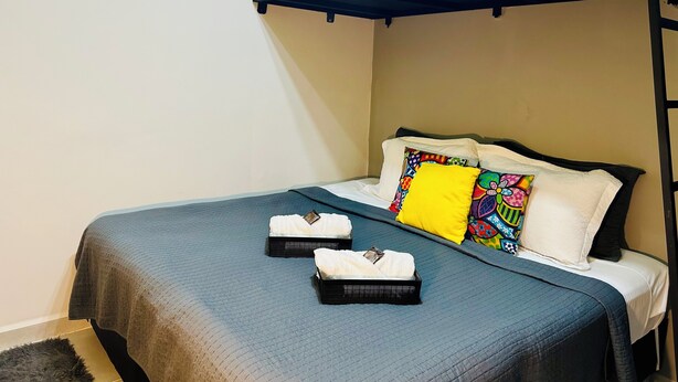 A bunk bed with a black frame, white pillows, and a colorful pillow. There are two black trays with white towels on the bed. - Nomad - Norte Sul, Cambui (Campinas)