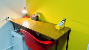 A small workspace with a wooden desk, a red chair, a lamp, and a basket containing snacks. - Nomad - Norte Sul, Cambui (Campinas)