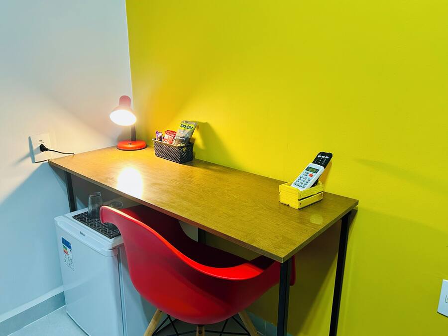 Un pequeño espacio de trabajo con un escritorio de madera, una silla roja, una lámpara y una cesta con aperitivos.