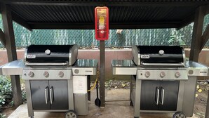 Zwei tragbare Gasgrills unter einem überdachten Bereich, im Hintergrund ein Metallzaun.