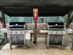 Two portable gas grills under a covered area with a metal fence in the background. - Sea and Sky Beachfront Condo, AC, Ocean Views, Sunrises, Steps to Beach! (Kapaʻa)