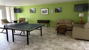 Ein Wohnzimmer mit Tischtennisplatte, zwei Sofas, einem Couchtisch und einem an der Wand montierten Fernseher.