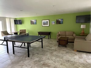 A living room with a ping pong table, two sofas, a coffee table, and a TV mounted on the wall.