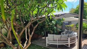 Eine Terrasse mit einer weißen Sitzgruppe im Freien, umgeben von üppigem Grün und einem Baum.