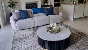Ein modernes Wohnzimmer mit einem grauen Sofa, einem runden Couchtisch und einer Küche im Hintergrund.