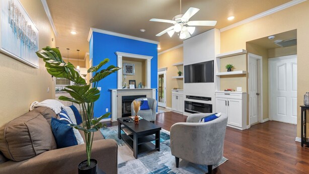 A living room with a fireplace, a television, and a kitchen area with white cabinets and a black countertop. - Your Home Away from Home  (Lowell)