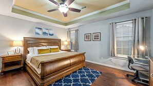 A bedroom with a wooden bed, nightstands, a desk with a chair, and a ceiling fan. - Your Home Away from Home  (Lowell)