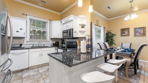 A kitchen with white cabinets, a granite countertop, a built-in microwave, and a dining area with a table and chairs. - Your Home Away from Home  (Lowell)