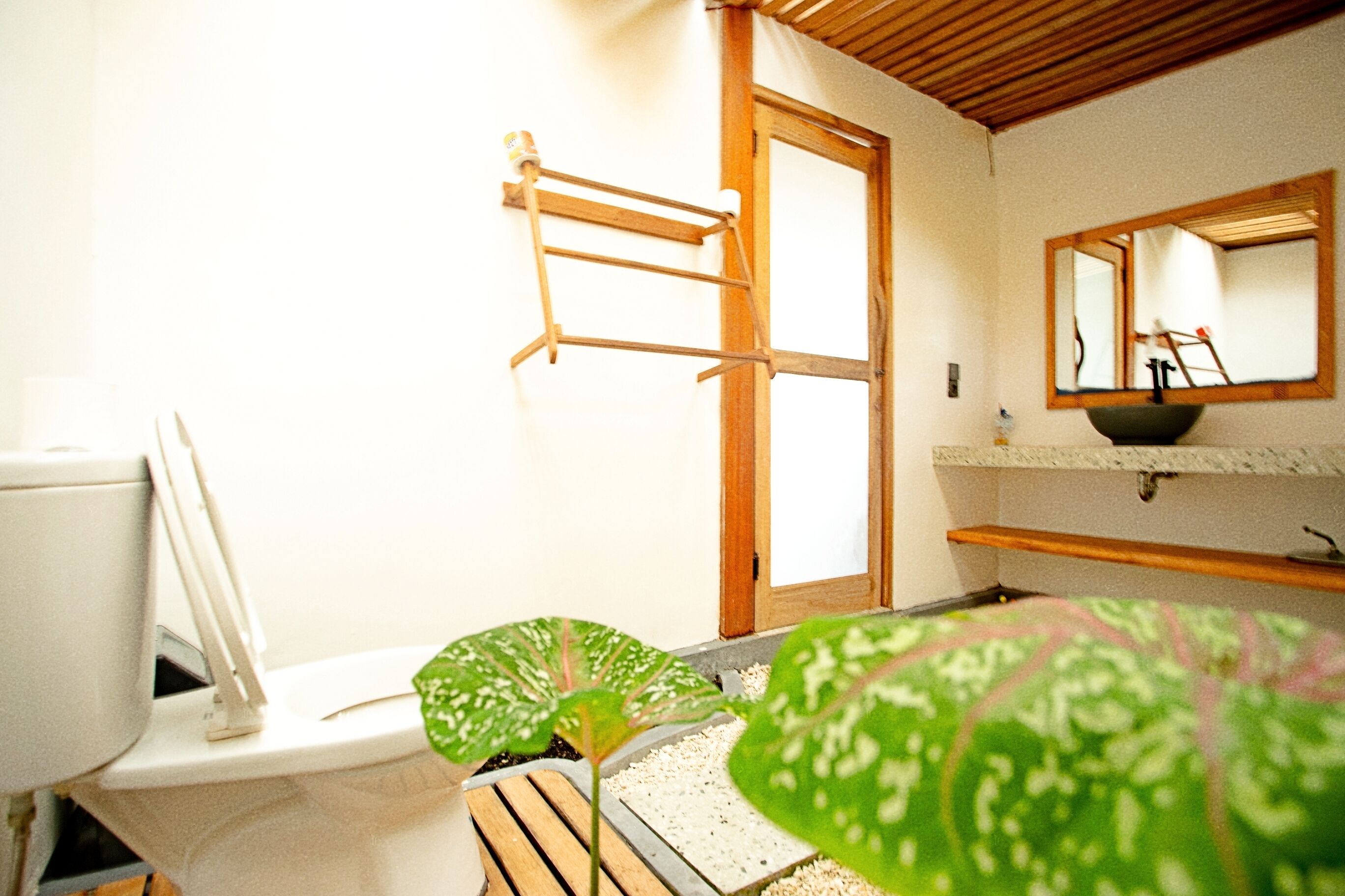 A bathroom with a toilet, a wooden shelf, a mirror, and a plant.