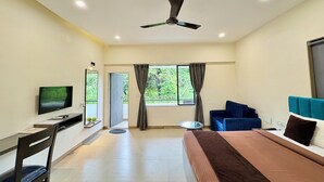 Ein modernes Hotelzimmer mit Bett, Schreibtisch mit Computer, Fernseher, Deckenventilator und einem Fenster mit Vorhängen.
