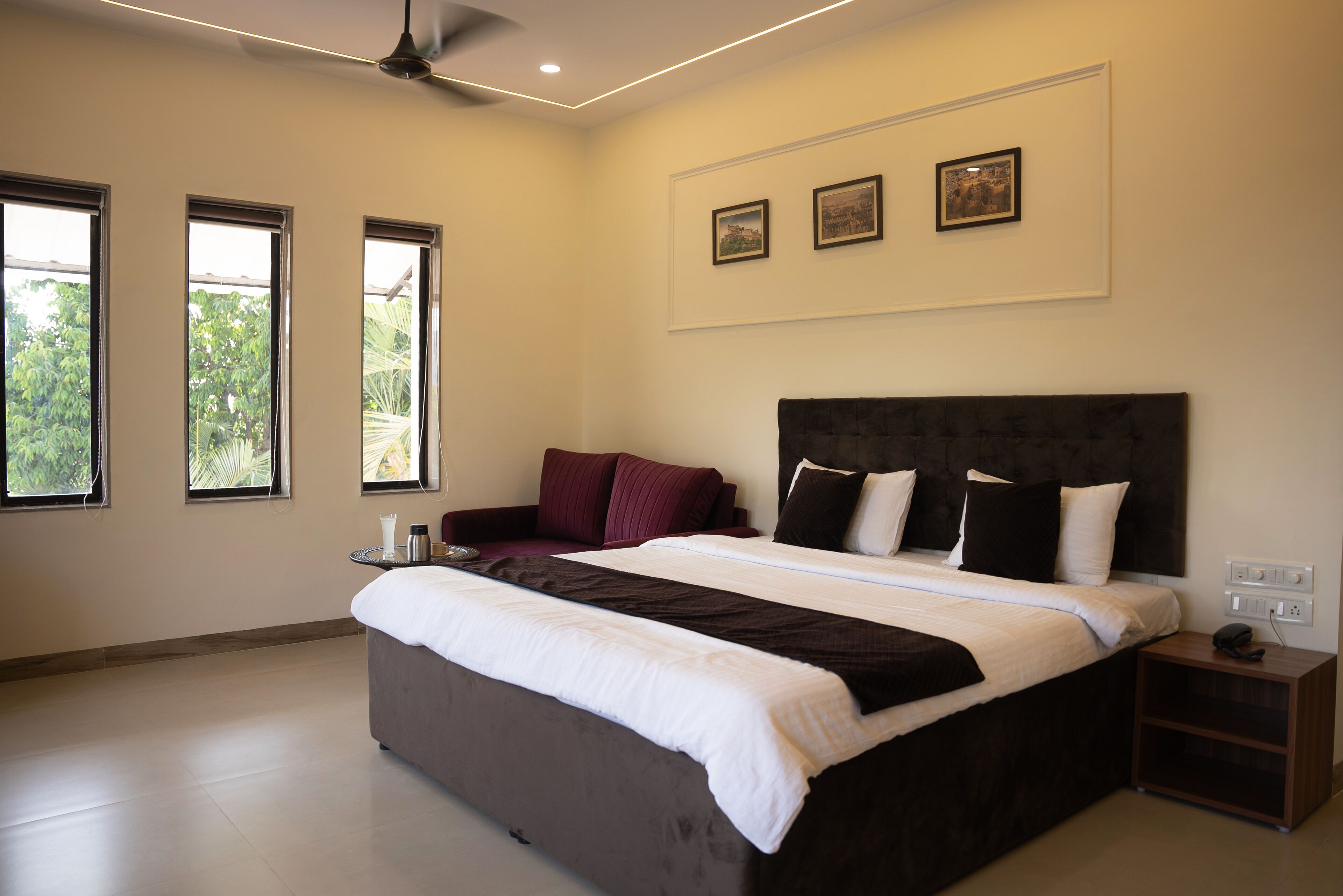 A modern bedroom with a large bed, a bedside table, and three windows.