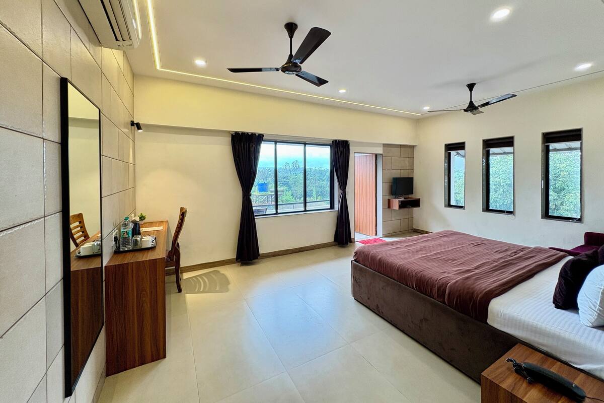 A modern hotel room with a large bed, a ceiling fan, a TV, and a window with curtains.