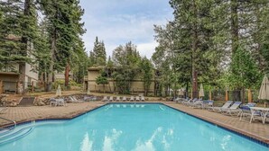 A rectangular swimming pool surrounded by lounge chairs and trees, with a brick deck and a no-swimming sign.