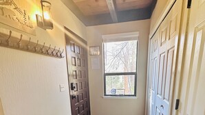 A hallway with a bench, a door with a keypad lock, a window with a view of trees, and a wall-mounted light fixture.