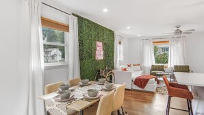 A modern living room with a dining area, white furniture, a green wall, and a sign that says "THIS MUST BE THE PLACE". - Game Room, Balcony, Fire Pit, 5 Bed, 4 Bath, WFH (Charlotte)