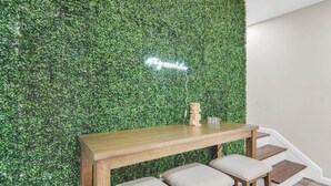 A wooden table with three stools against a wall covered in green foliage, with a neon sign above. - Game Room, Balcony, Fire Pit, 5 Bed, 4 Bath, WFH (Charlotte)