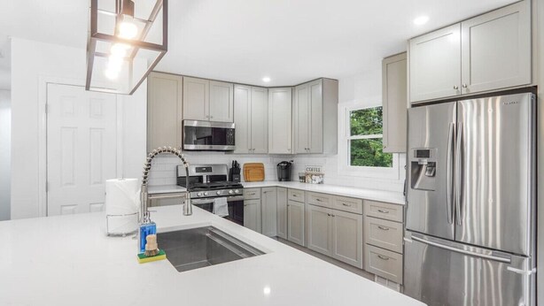 A modern kitchen with white cabinets, stainless steel appliances, and a large island with a sink. - Game Room, Balcony, Fire Pit, 5 Bed, 4 Bath, WFH (Charlotte)