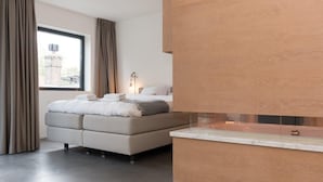 Une chambre moderne avec un grand lit, une baignoire intégrée et une fenêtre avec des rideaux.