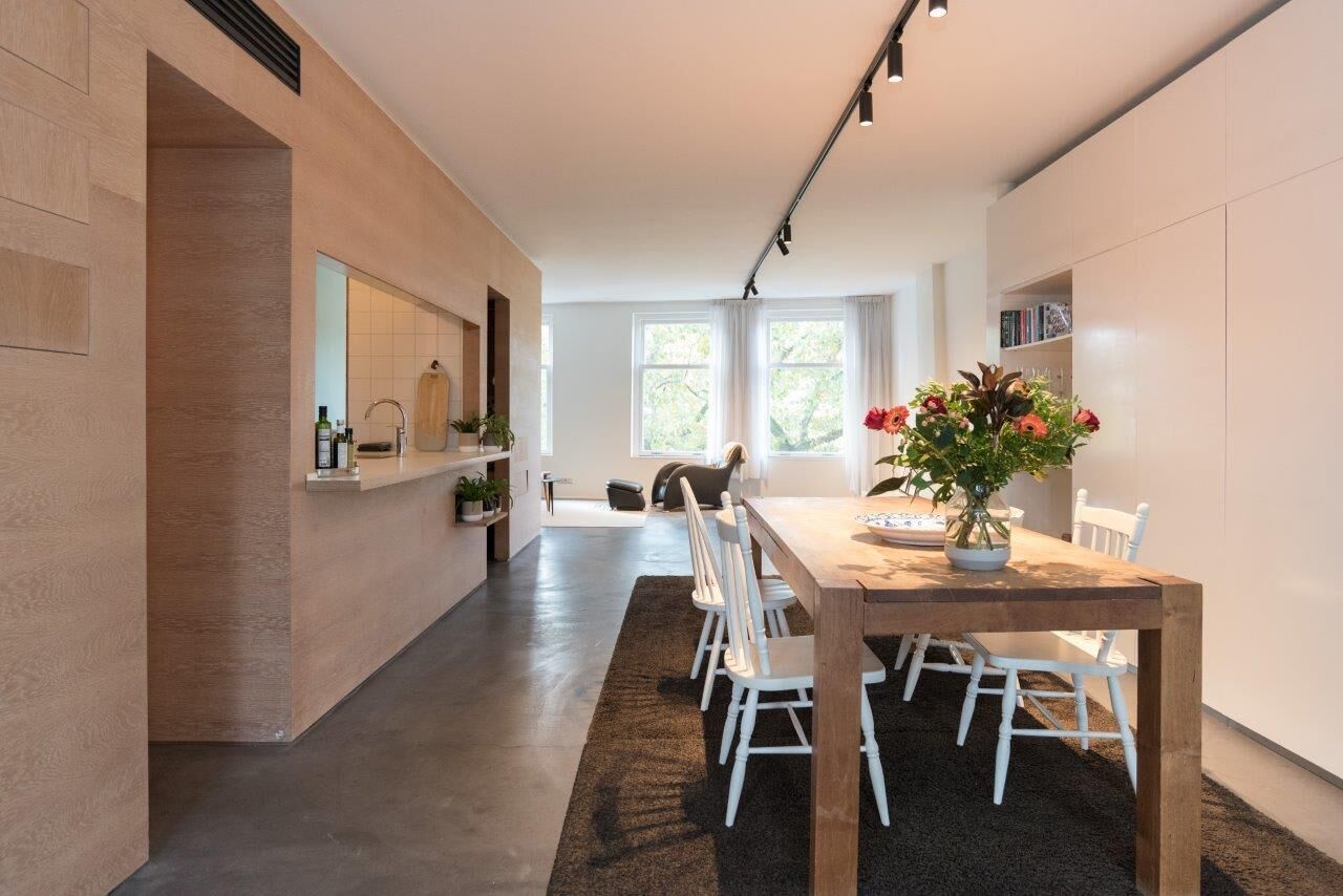 Une cuisine moderne avec un îlot central, des chaises blanches et une table à manger agrémentée d’un vase de fleurs.