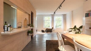 Une cuisine moderne avec un plan de travail en bois, un coin repas comprenant une table et des chaises, et une grande fenêtre agrémentée de rideaux.