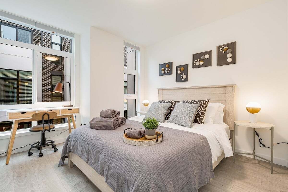 A modern bedroom with a large bed, a desk, and a window.