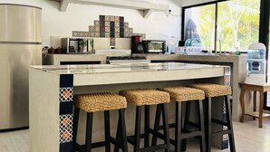 Eine moderne Küche mit einer zentralen Kochinsel, Barhocker, einem Kühlschrank, einer Mikrowelle und einer Kaffeemaschine.
