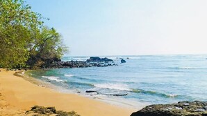 Ein Strand mit klarem, blauem Wasser, sandigem Ufer und Felsenformationen.