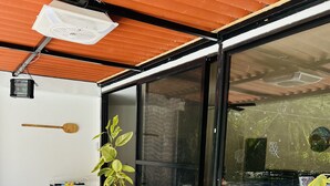 Ein modernes Wohnzimmer mit Holzmöbeln, einem großen Fenster und einem Deckenventilator.