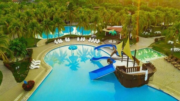 Ein Pool mit einer Piratenschiff-Rutsche, umgeben von Palmen und Liegestühlen.