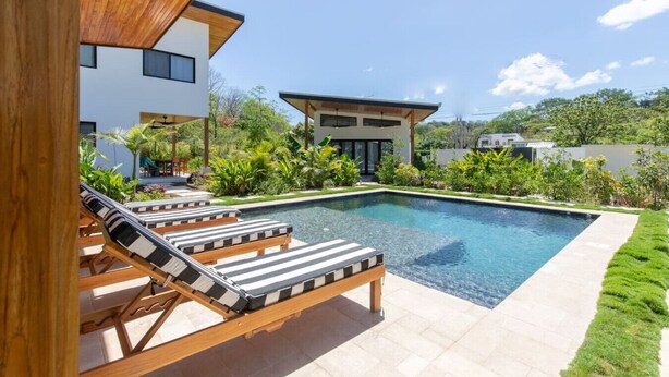 Una casa moderna con piscina, sillas de descanso y un jardín bien cuidado.