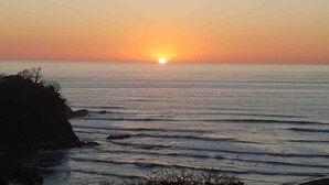 Un atardecer sobre un mar tranquilo con costa rocosa.