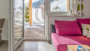 Een kamer met een schuifglasdeur die uitkomt op een besneeuwde omgeving, een houten pergola en een bed met roze beddengoed.