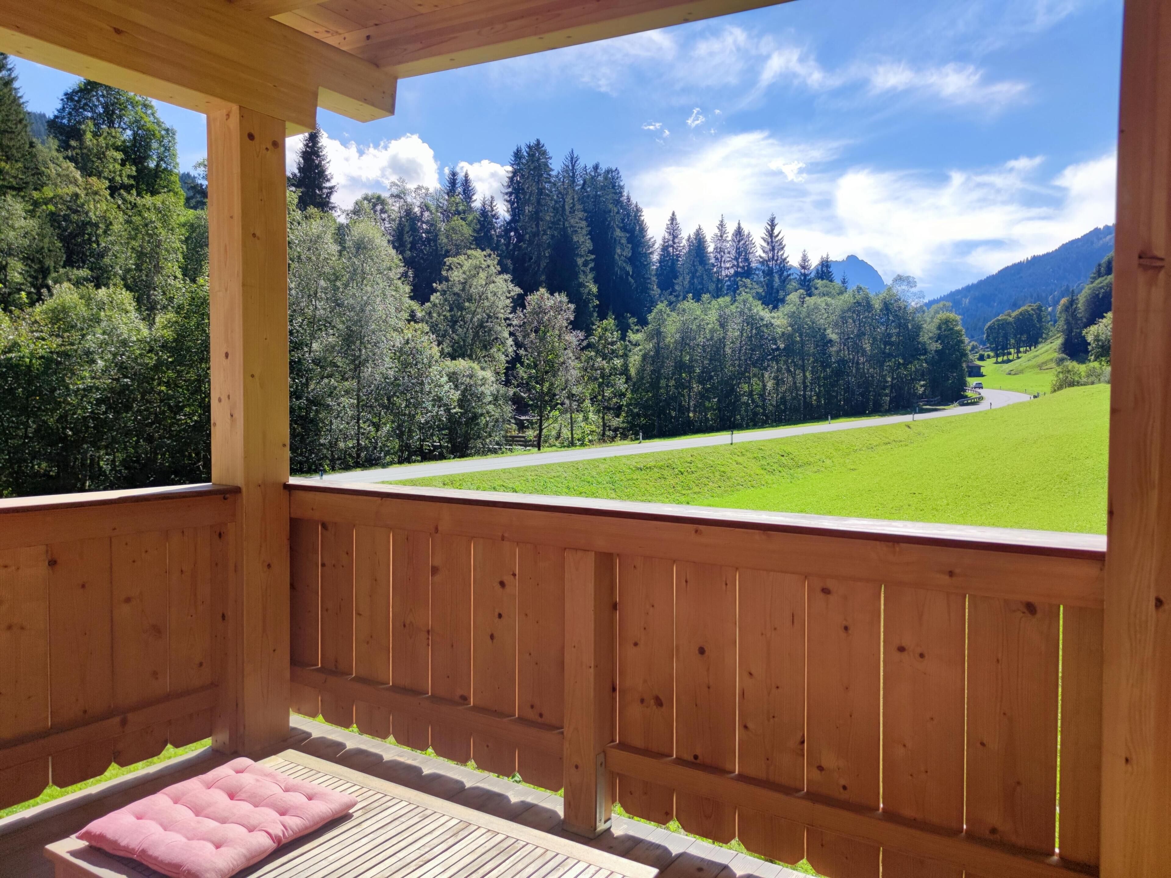 Un balcon en bois donnant sur un champ verdoyant et des arbres.
