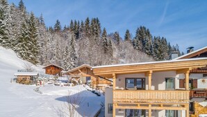 Een houten chalet met balkon, omgeven door met sneeuw bedekte bomen en een heldere lucht.