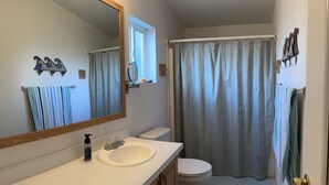 Une salle de bain avec un lavabo blanc, un miroir, des toilettes et un rideau de douche.