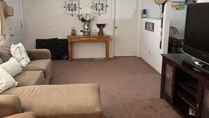 Un salon avec un ventilateur de plafond, un canapé, une table basse et un téléviseur posé sur un meuble.