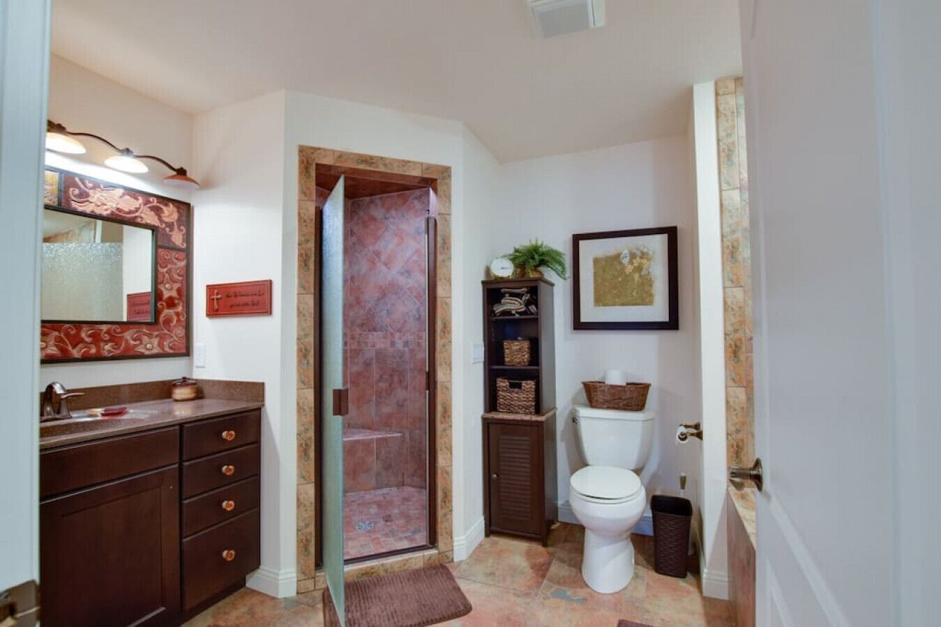 A bathroom with a wooden vanity, a glass shower enclosure, a toilet, and a shelf with baskets.