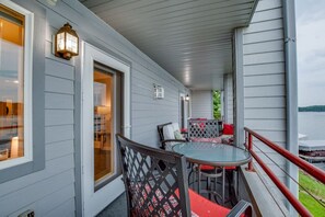 A covered porch with a glass table and chairs, a red railing, and a view of a lake.