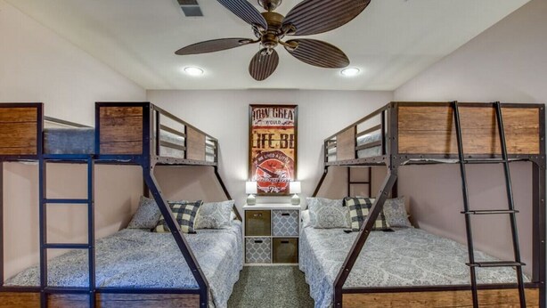 A dormitory room with bunk beds, a ceiling fan, a poster on the wall, and a small cabinet.
