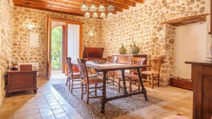 A rustic dining area with a stone wall, wooden ceiling beams, and a table set for four. - Sa Bisbal by Interhome (Moscari)