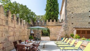 An outdoor patio with a table set for dining, surrounded by stone walls and a row of yellow lounge chairs. - Sa Bisbal by Interhome (Moscari)