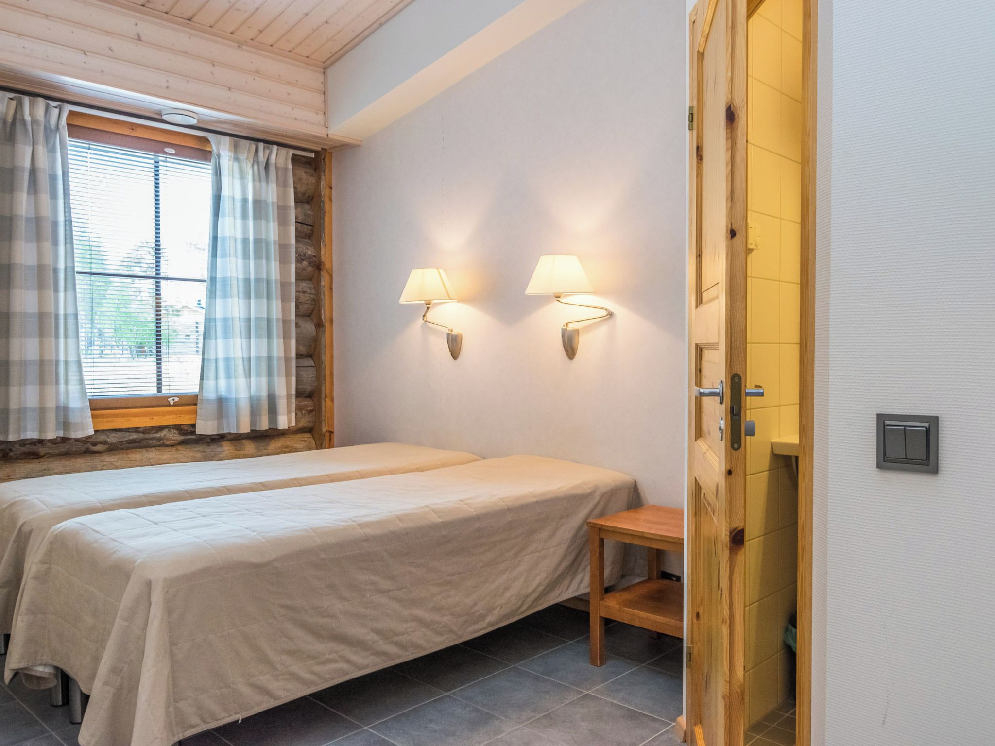 A bedroom with two beds, a window with curtains, and two wall-mounted lamps.