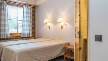 A bedroom with two beds, a window with curtains, and two wall-mounted lamps.