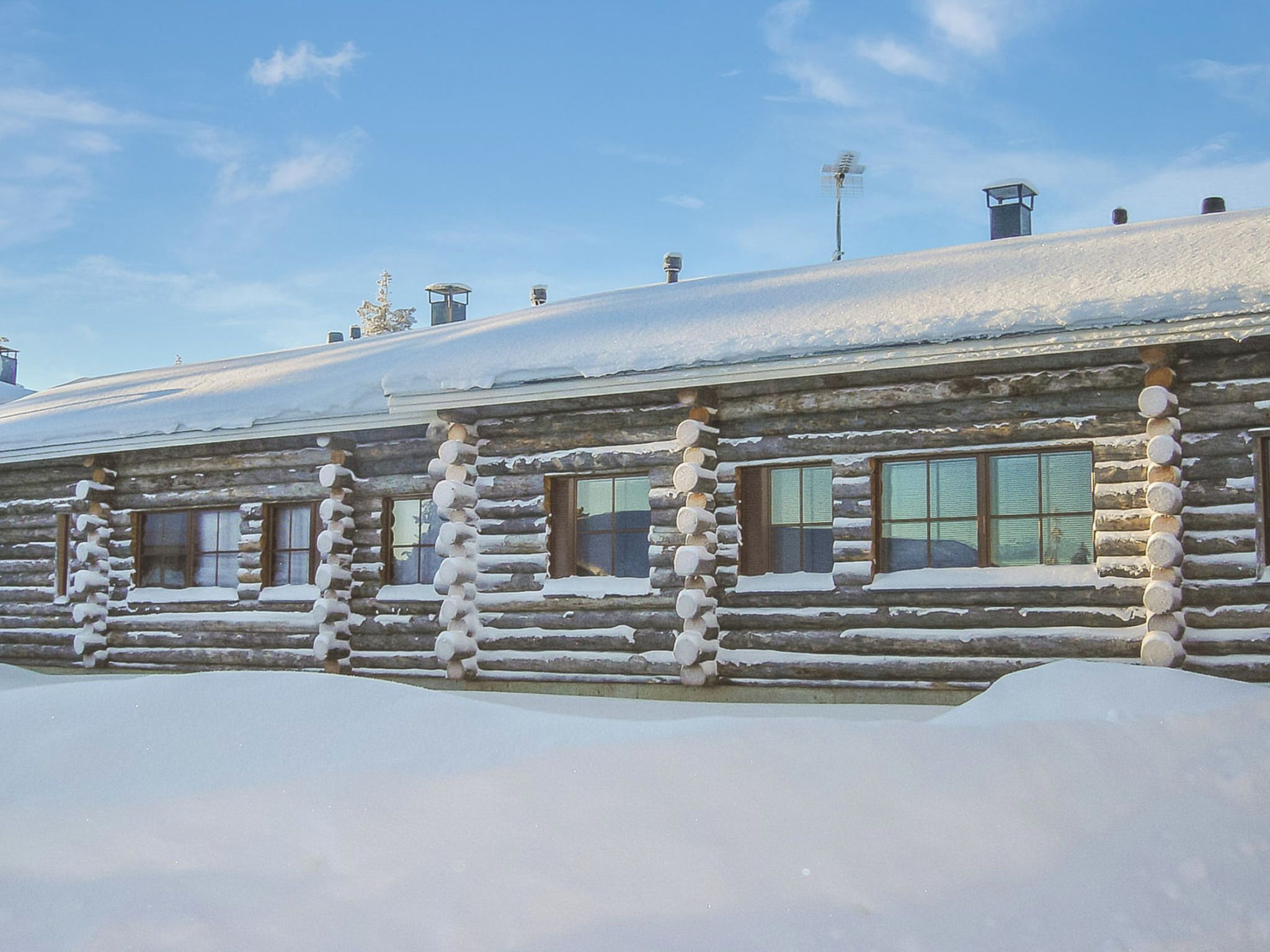 A log cabin with a snow-covered roof and windows, surrounded by snow.
