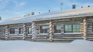 A log cabin with a snow-covered roof and windows, surrounded by snow.