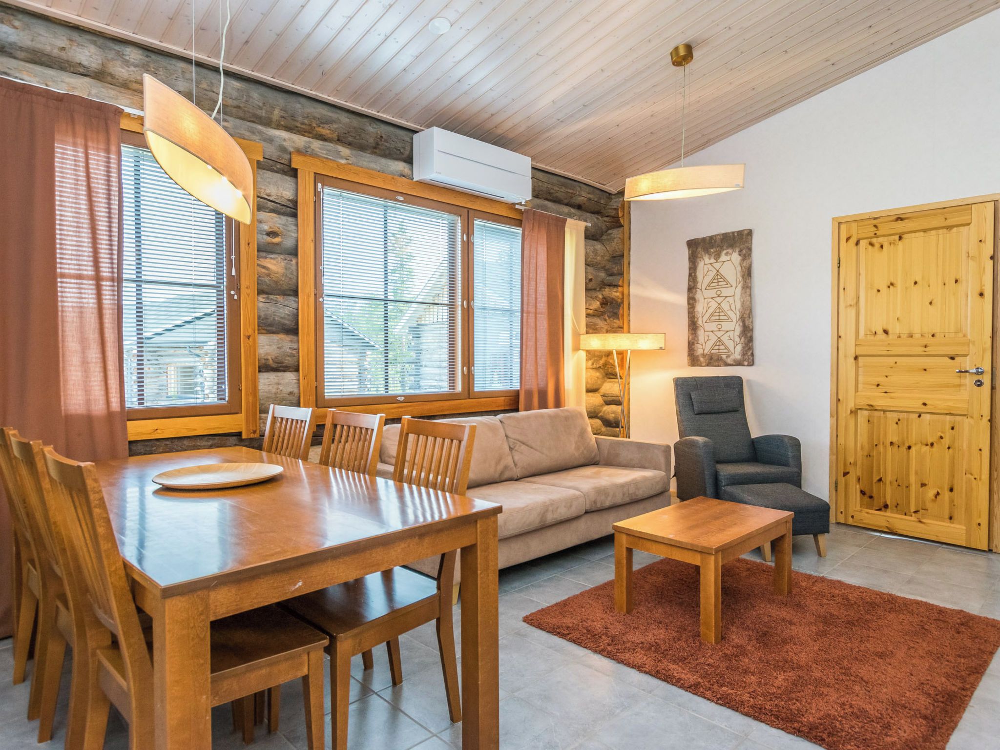 Un salon chaleureux avec une table à manger en bois, un canapé et un fauteuil, une cheminée et une porte en bois.