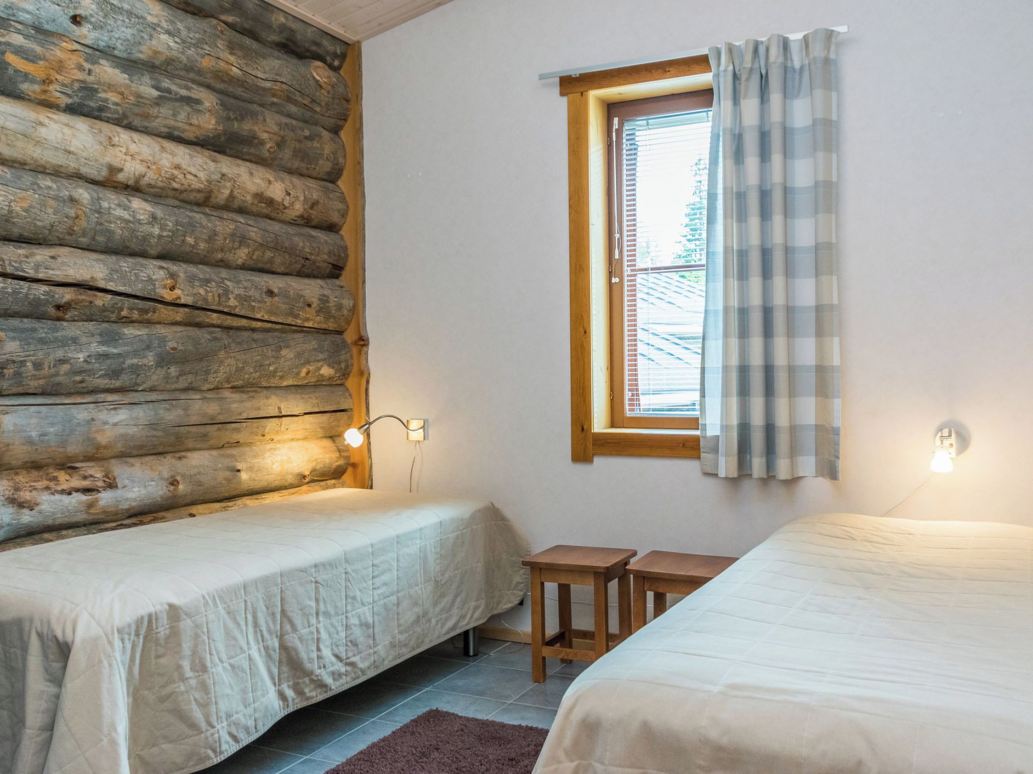 A room with two beds, a window with a curtain, and a wall with a log pattern.