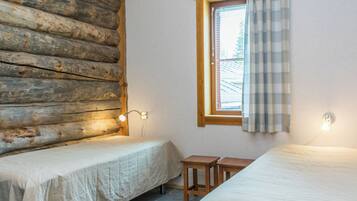 A room with two beds, a window with a curtain, and a wall with a log pattern.