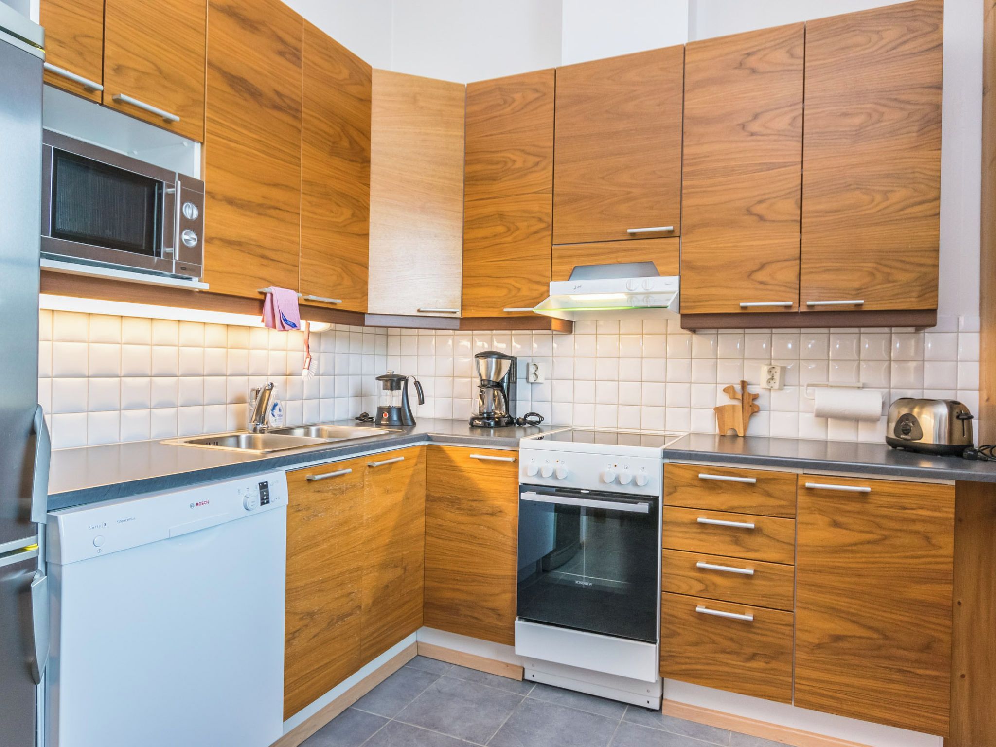 Une cuisine moderne avec des meubles en bois, un four à micro-ondes encastré, un lave-vaisselle Bosch et une cuisinière.