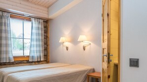 Een kamer met twee bedden, een raam met gordijnen, twee wandlampen, een houten deur en een kleine tafel.